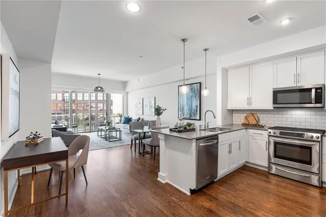 a open kitchen with stainless steel appliances granite countertop a stove top oven a sink dishwasher a dining table and chairs with wooden floor