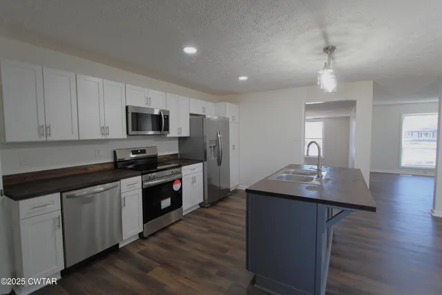 a kitchen with kitchen island granite countertop stainless steel appliances a sink cabinets and wooden floor