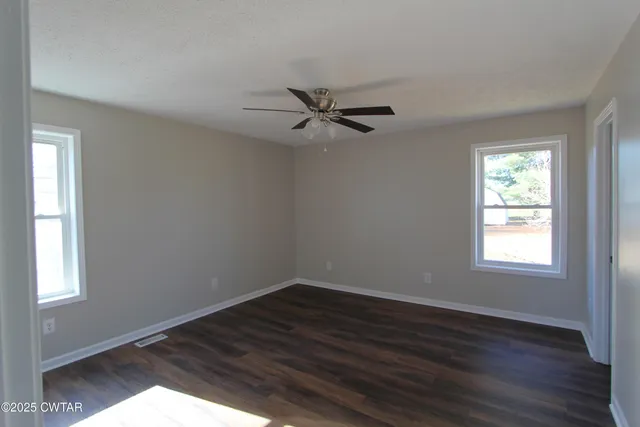 a view of a livingroom with a hardwood floor a ceiling fan and windows