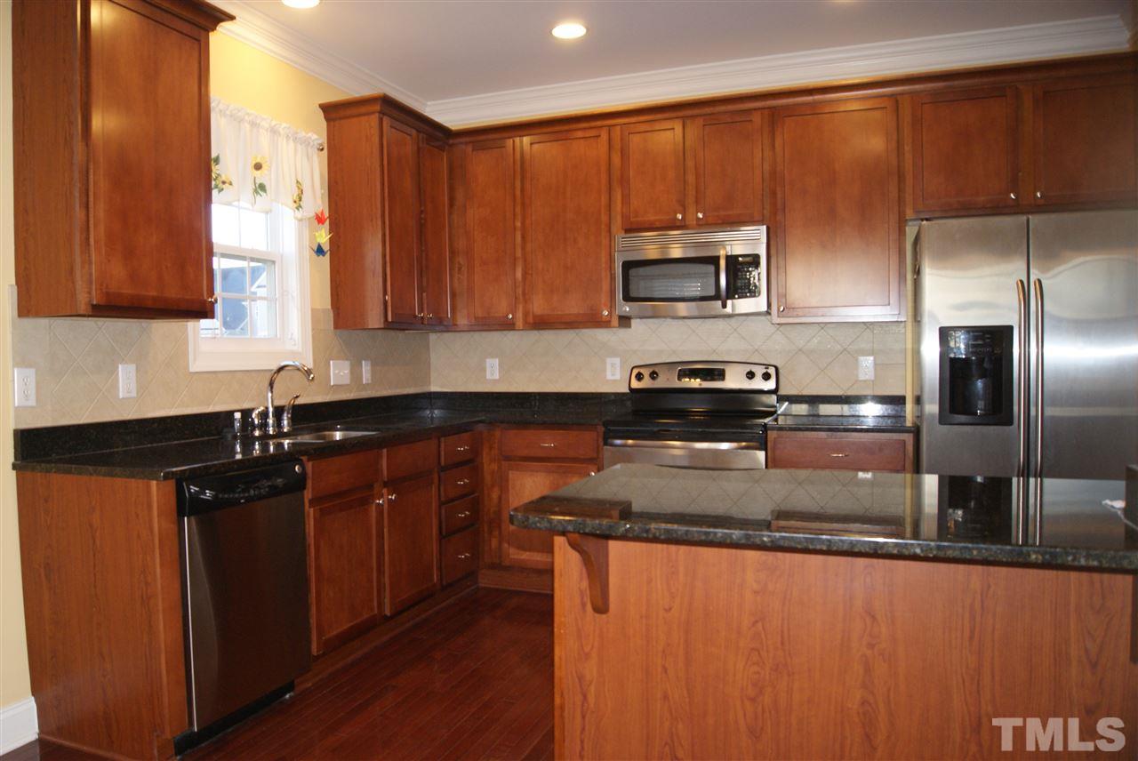 642 Democracy Street Raleigh, NC 27603 - Photo 8 of 25 a kitchen with stainless steel appliances granite countertop a sink a stove a refrigerator a microwave oven with wooden cabinets and floor
