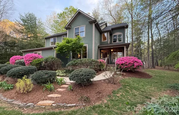 a view of a house in front of a yard with potted plants and large trees