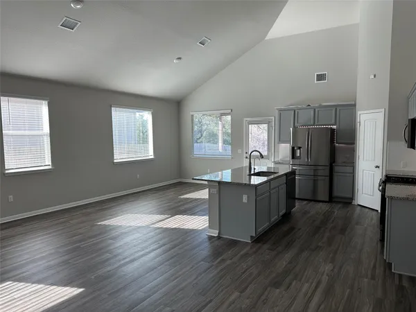 a living room with stainless steel appliances furniture wooden floor and a kitchen view