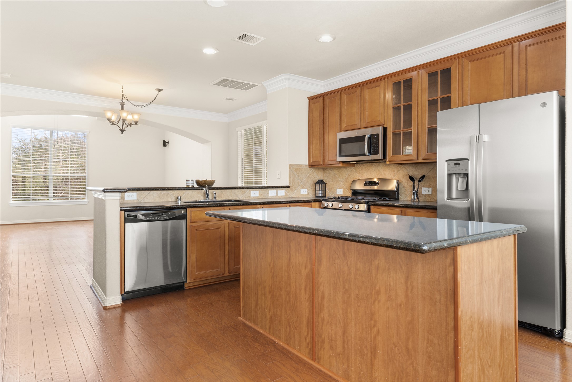 3334 Clearview Villa Way Houston, TX 77025 - Photo 10 of 35 This photo showcases a modern kitchen with stainless steel appliances, wooden cabinets, and a large island with granite countertops. The open layout flows into a bright dining area with hardwood floors and ample natural light from large windows.