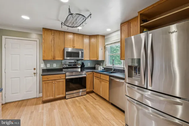 a kitchen with stainless steel appliances granite countertop a refrigerator a sink dishwasher a stove and a dining table with wooden floor