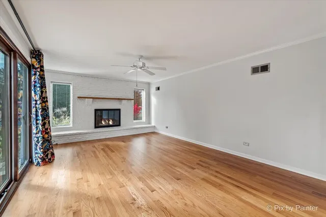 a view of an empty room with wooden floor fireplace and a window