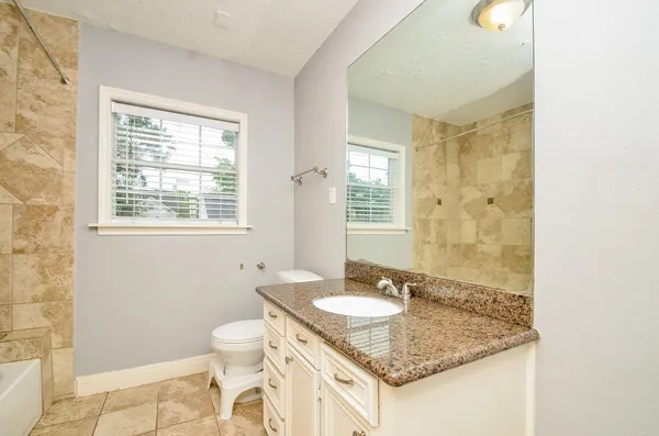 a bathroom with a granite countertop sink a toilet a mirror and a window