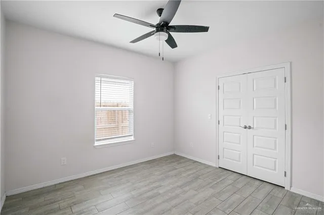 an empty room with wooden floor ceiling fan and windows