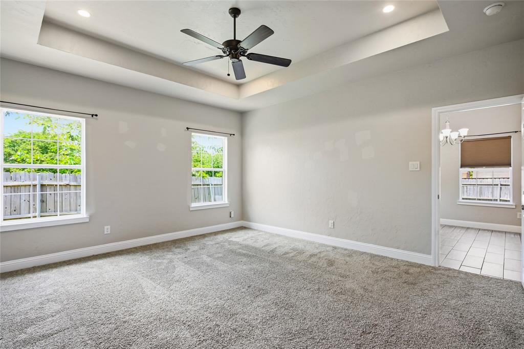 1502 Reed Street Greenville, TX 75401 - Photo 15 of 26 Spacious room featuring a tray ceiling with recessed lighting and a ceiling fan, two large windows, plush carpet flooring, and a doorway opening to a room with tile flooring