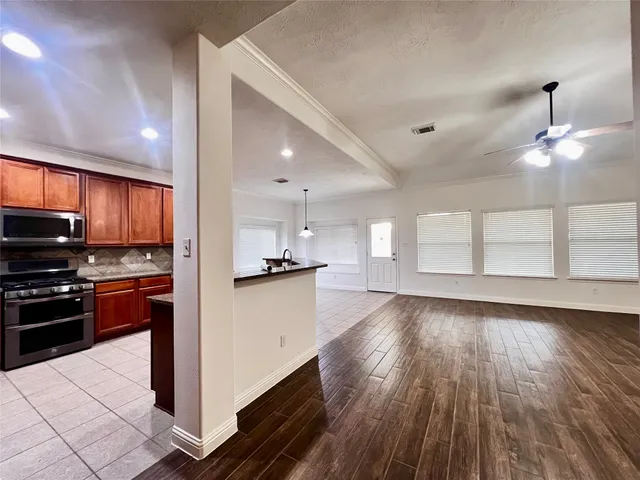 a kitchen with stainless steel appliances kitchen island granite countertop a stove a refrigerator a sink a microwave oven with wooden floor and cabinets