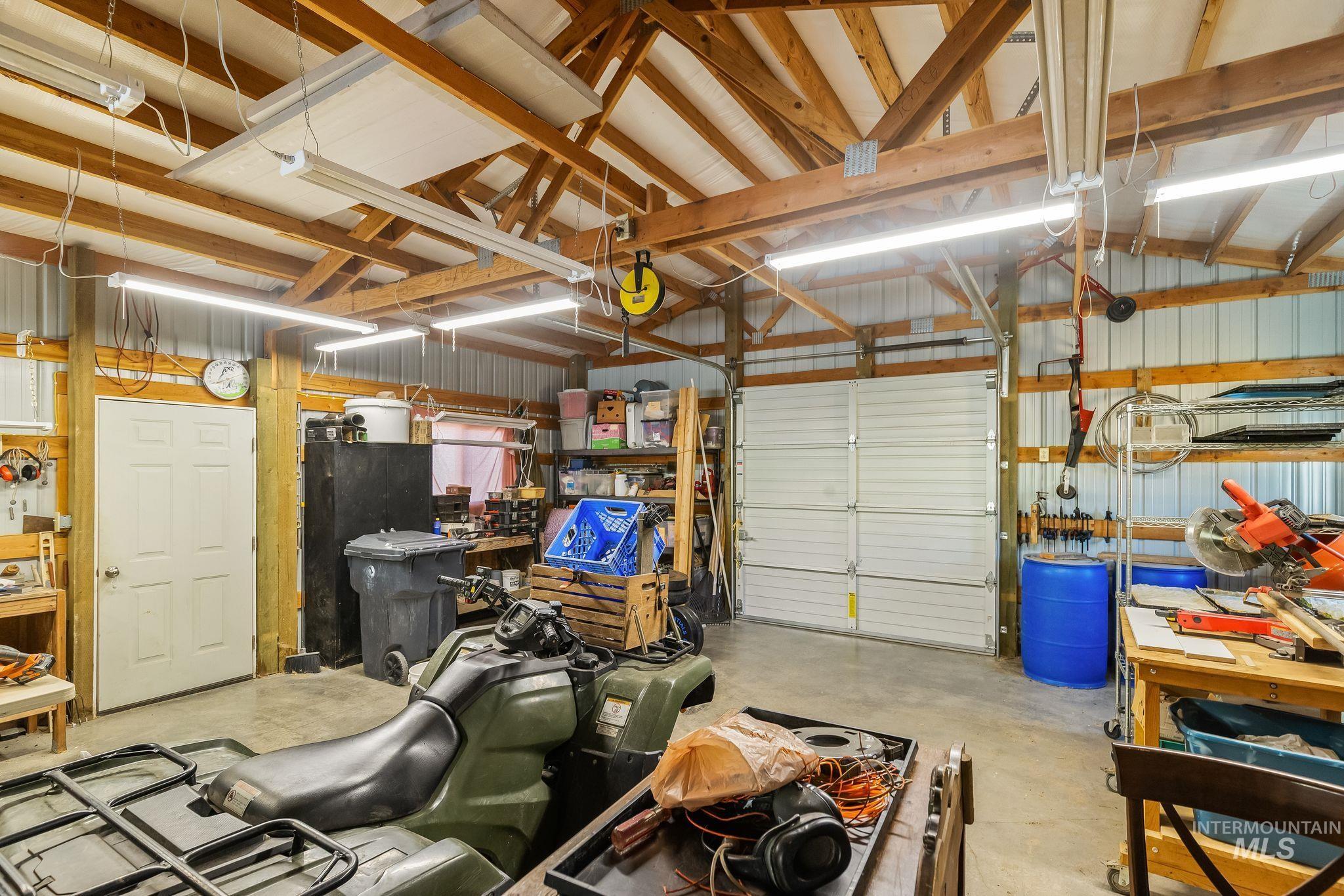 4935 Lenville Road Moscow, ID 83843 - Photo 42 of 49 Spacious garage featuring a concrete floor, exposed wood beam ceiling, multiple fluorescent light fixtures, and a large roll-up garage door