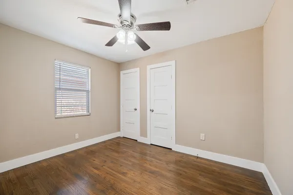 an empty room with wooden floor chandelier fan and windows