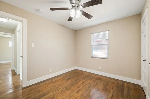 an empty room with wooden floor chandelier fan and windows
