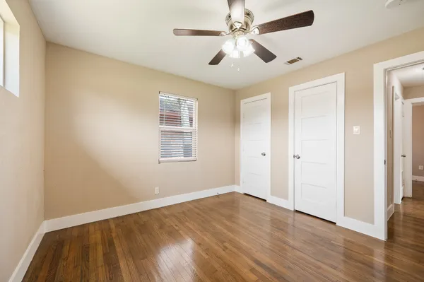 an empty room with wooden floor ceiling fan and windows