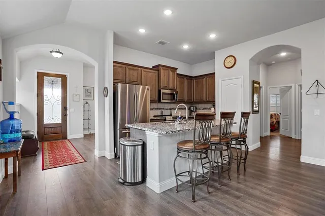 a kitchen with stainless steel appliances a refrigerator a stove top oven and a dining table with wooden floor