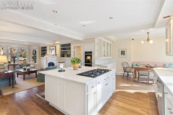 a large white kitchen with stainless steel appliances granite countertop a stove oven a dining table and chairs with wooden floor