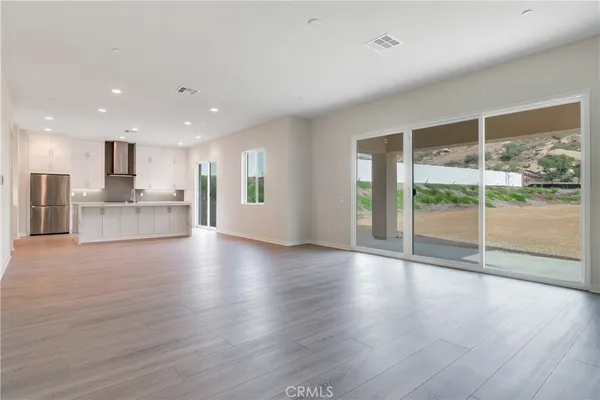 a view of an empty room with wooden floor and a kitchen
