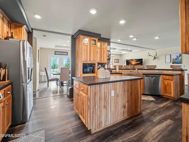 a kitchen with stainless steel appliances granite countertop a refrigerator a sink dishwasher a stove and a dining table with wooden floor