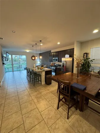 a room with stainless steel appliances kitchen island granite countertop a dining table chairs and a refrigerator