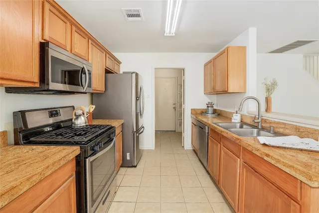 a kitchen with stainless steel appliances granite countertop a stove top oven a sink and dishwasher a refrigerator with wooden cabinets