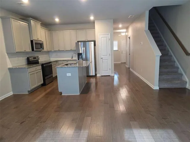 a kitchen with stainless steel appliances granite countertop a refrigerator a sink dishwasher a stove top oven a refrigerator and white cabinets with wooden floor