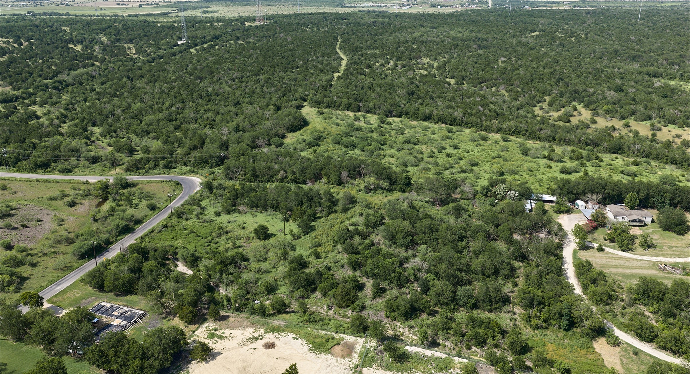 1400 Williamson Road Kyle, TX 78640 - Photo 9 of 13 Vast, undeveloped acreage with winding roads and distant structures, offering potential for expansion.