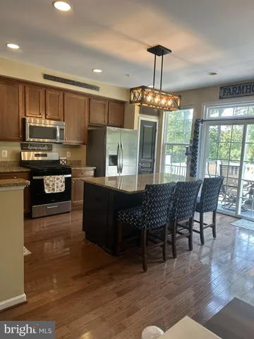 a kitchen with stainless steel appliances granite countertop a stove top oven a refrigerator a kitchen island a dining table and chairs with wooden floor