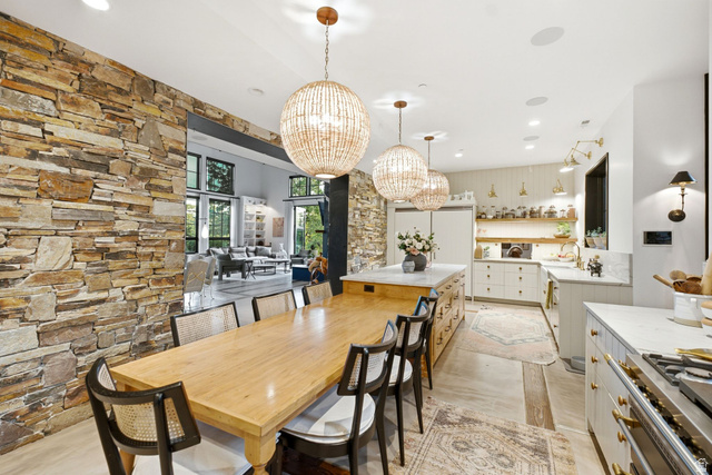 5971 Maple Ridge Trail Oakley, UT 84055 - Photo 15 of 43 Open-concept dining and kitchen area featuring a stone accent wall, three spherical beaded pendant lights, a gas range with a substantial hood, and extensive cabinetry with gold-toned hardware