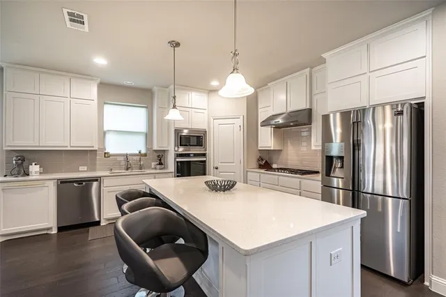 a kitchen with stainless steel appliances granite countertop a sink a stove a refrigerator and island with wooden floor