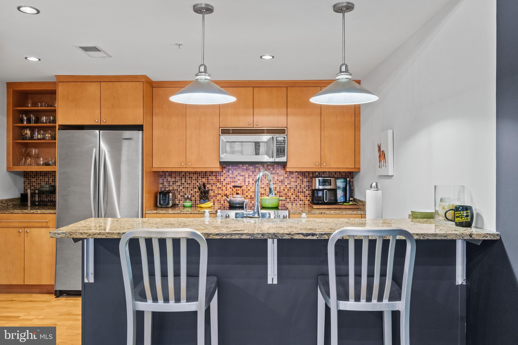 850 Aliceanna Street, Unit 604 Baltimore, MD 21202 - Photo 13 of 43 a kitchen with stainless steel appliances granite countertop a stove a refrigerator a kitchen island a sink dishwasher a dining table and chairs with wooden floor