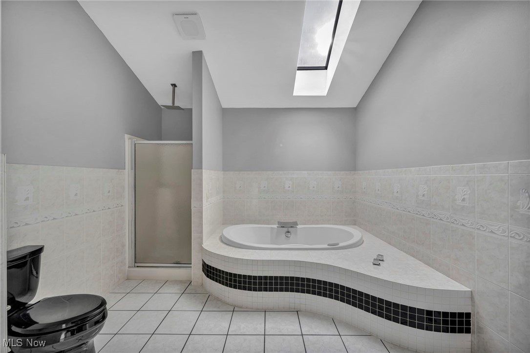 20202 Sumpter Road Cleveland, OH 44128 - Photo 27 of 46 Bathroom featuring tile walls, light tile patterned floors, a bath, a shower stall, and a skylight