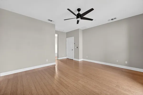 an empty room with wooden floor ceiling fan and windows