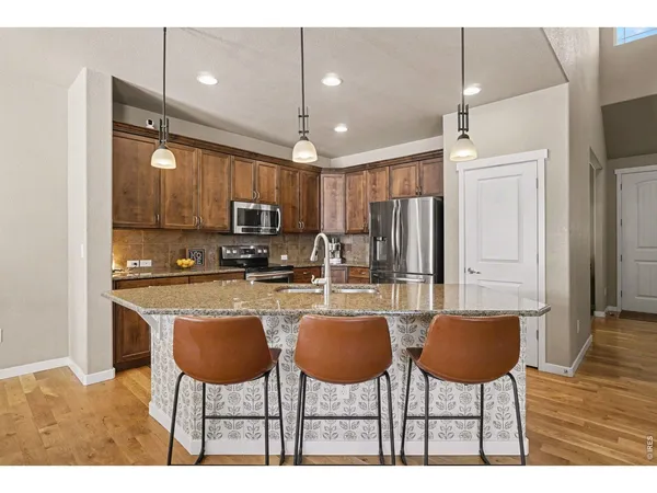 a kitchen with stainless steel appliances kitchen island granite countertop a dining table chairs refrigerator and microwave