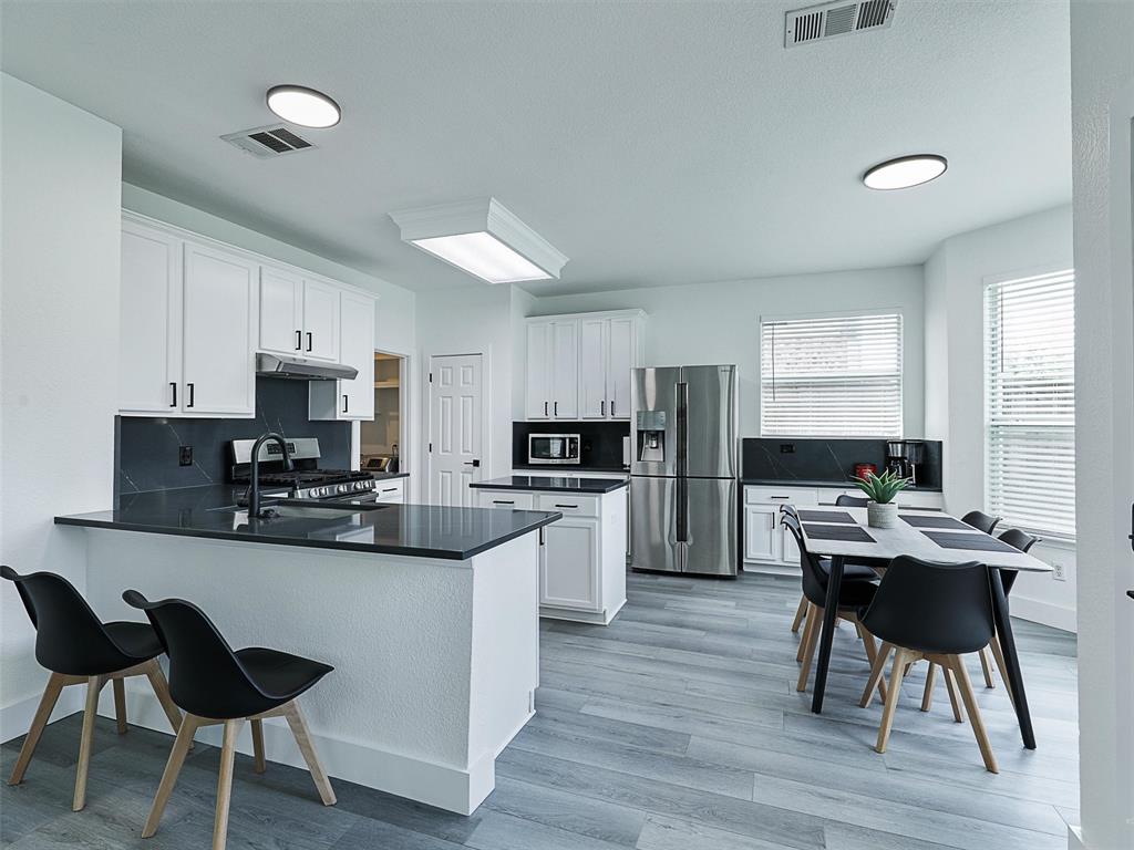 6229 Bear Run Road The Colony, TX 75056 - Photo 20 of 25 a kitchen with stainless steel appliances kitchen island granite countertop a table chairs microwave and sink