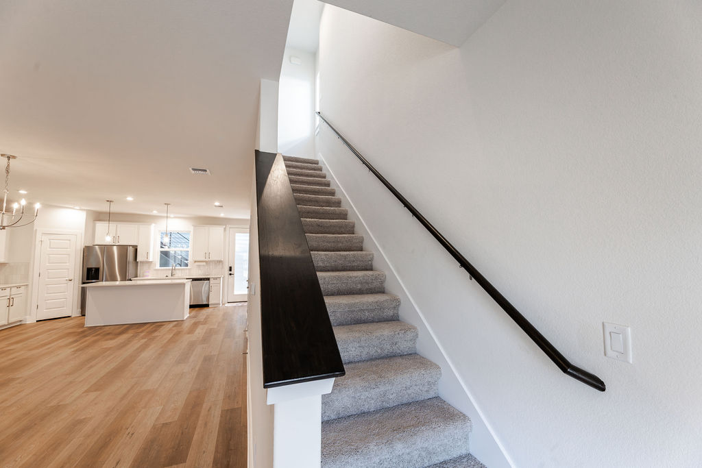 6414 Cowman Way Austin, TX 78747 - Photo 35 of 35 Carpeted stairs ascend from a modern open-concept floor plan highlighted by wood flooring.