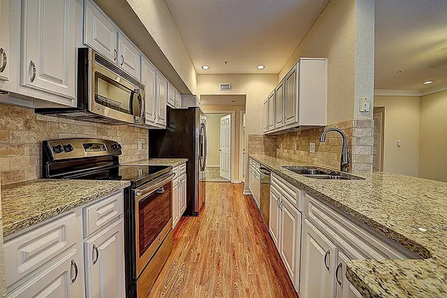 a kitchen with stainless steel appliances granite countertop a stove top oven a sink dishwasher a refrigerator and cabinets with wooden floor