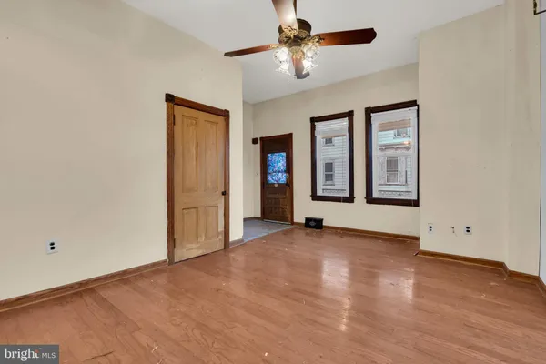 an empty room with wooden floor chandelier fan and windows