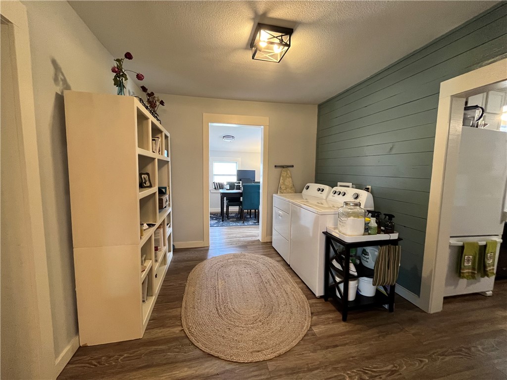1102 North Travis Avenue Cameron, TX 76520 - Photo 19 of 48 Laundry area featuring a textured ceiling, wood walls, dark wood-style floors, and washer and clothes dryer