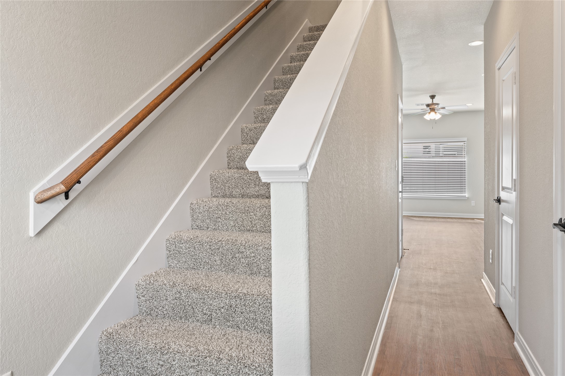 14010 Longstreet Road, Unit 2 Willis, TX 77318 - Photo 26 of 29 This photo showcases a modern, well-lit hallway with a carpeted staircase featuring a wooden handrail. The space leads to an open area with a ceiling fan and a window with blinds, offering a clean and inviting entryway.