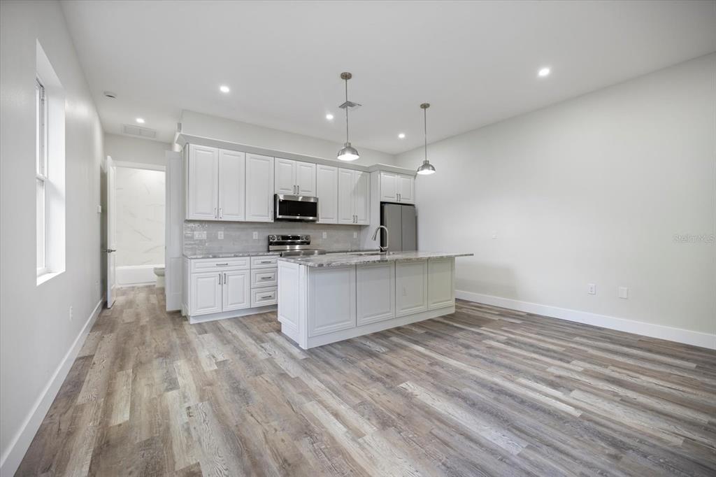 3525 McIntosh Road Sarasota, FL 34232 - Photo 15 of 40 a large white kitchen with kitchen island a sink dishwasher a stove and white cabinets with wooden floor
