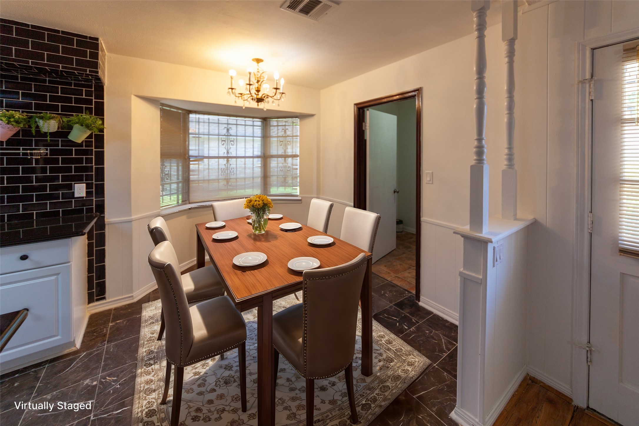 8826 Roos Road Houston, TX 77036 - Photo 10 of 42 This dining area features a cozy space with a modern wooden table set for six, complemented by elegant chairs. It has large bay windows for natural light, a stylish chandelier, and a decorative black tile backsplash on one wall. The room is inviting and perfect for intimate gatherings.