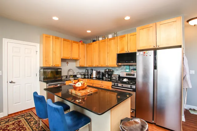 a kitchen with stainless steel appliances granite countertop a refrigerator a stove a sink a dining table and chairs with wooden floor