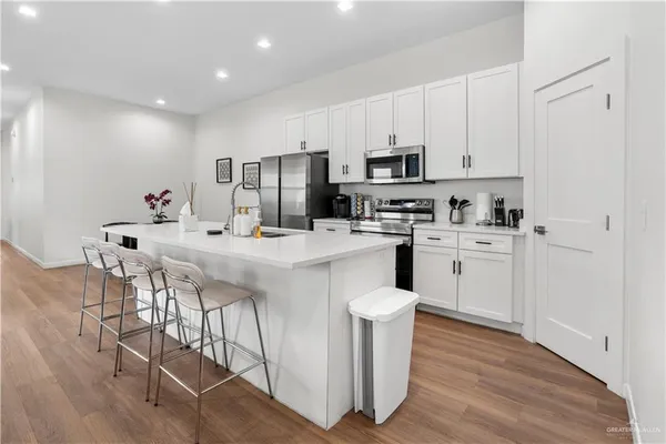 a kitchen with stainless steel appliances kitchen island granite countertop a stove a sink a refrigerator and white cabinets with wooden floor