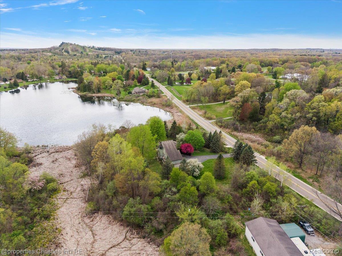 6175 Tripp Road Holly, MI 48442 - Photo 56 of 63 Aerial perspective showcasing a lakefront property with mature trees and direct access to a paved road
