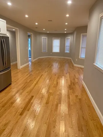 a view of an empty room with wooden floor and a kitchen