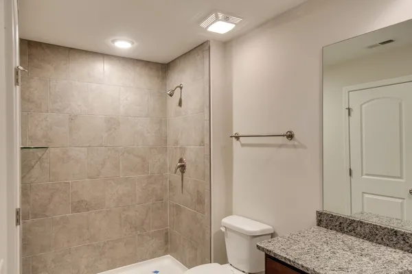 a bathroom with a granite countertop sink a toilet a mirror and shower