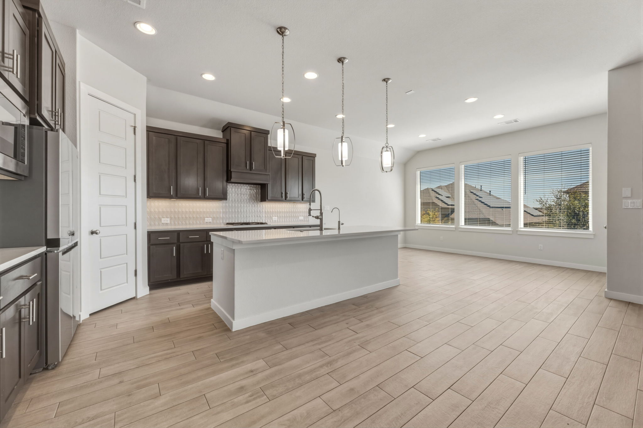 116 Tanali Trail Georgetown, TX 78628 - Photo 18 of 40 Kitchen with dark wood finish cabinets, a center island with sink, light stone counters, wood tiled floors, and pendant lighting