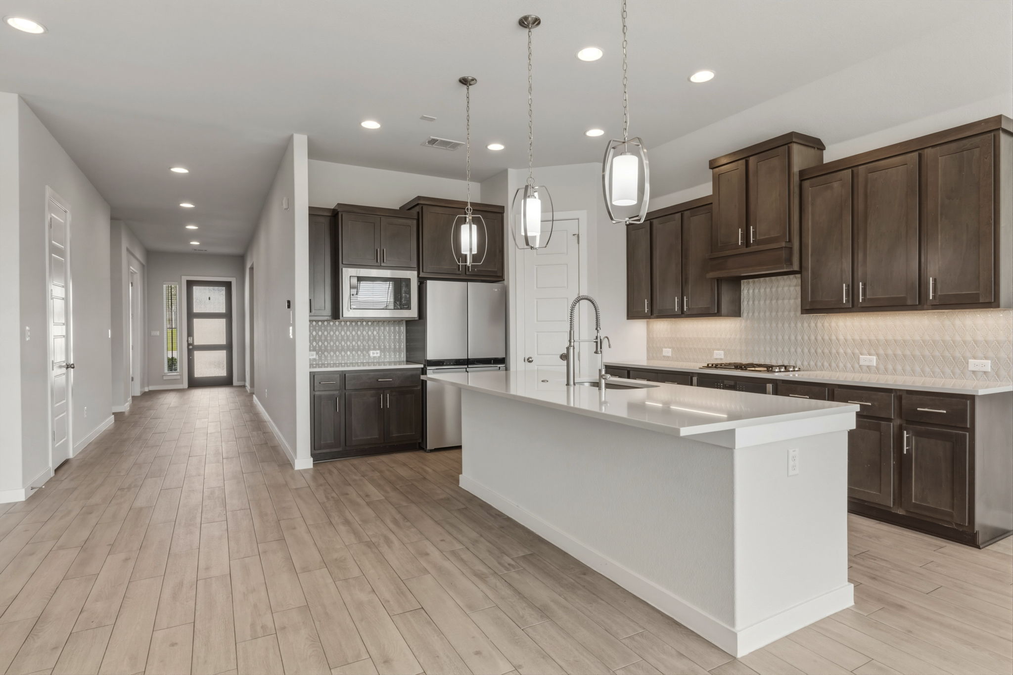 116 Tanali Trail Georgetown, TX 78628 - Photo 19 of 40 Kitchen with dark wood finish cabinetry, tasteful backsplash, stainless steel appliances, a center island with sink, and light stone countertops
