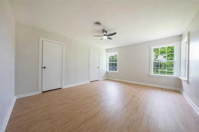 an empty room with wooden floor chandelier fan and windows