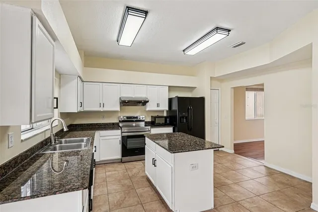 a kitchen with stainless steel appliances granite countertop a stove top oven a sink a refrigerator and white cabinets