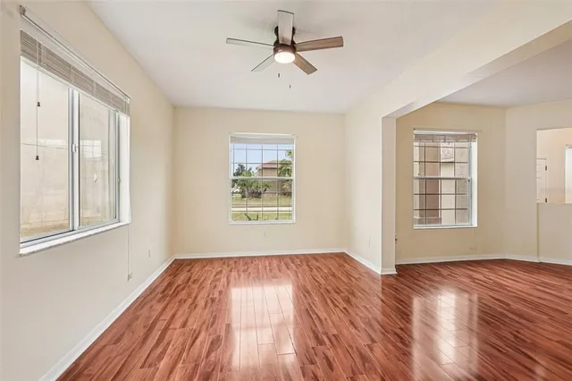 an empty room with wooden floor chandelier fan and windows